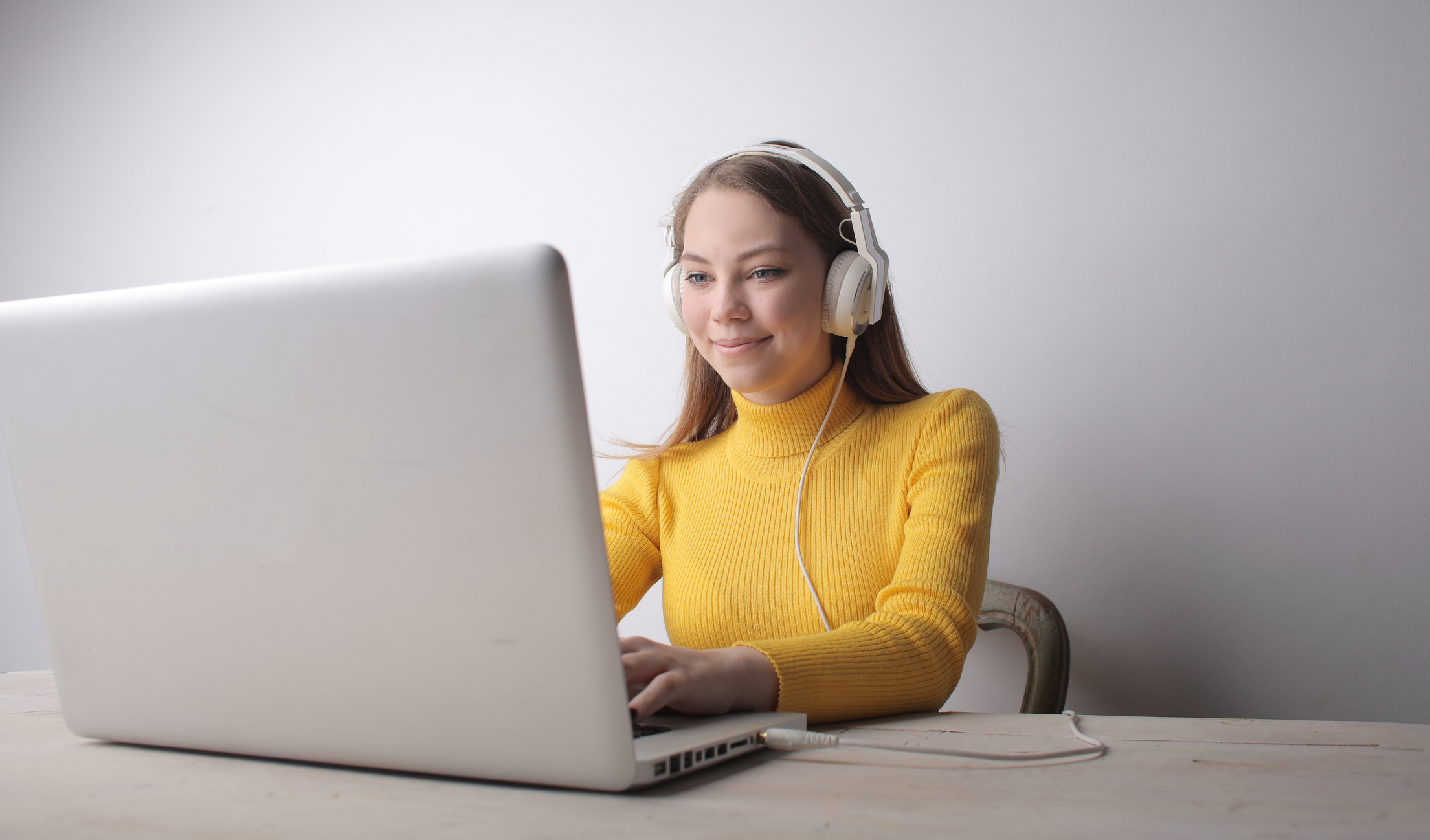 Woman in Yellow Sweater Wearing Headphones Using Laptop